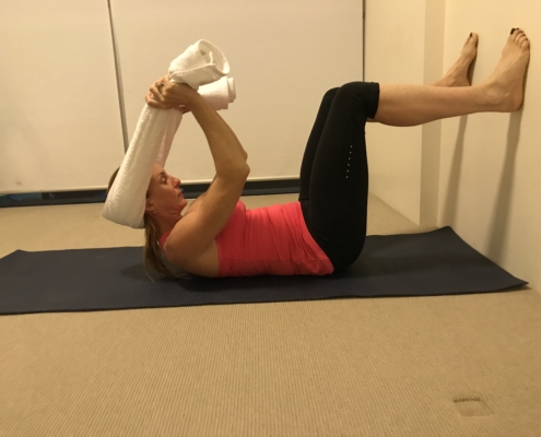 4B a picture of woman lying on her back with her feet on the wall and stretching her neck with a towel