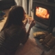 a lady lying on her stomach and holding a cup in front of a fireplace