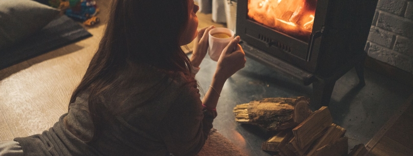 a lady lying on her stomach and holding a cup in front of a fireplace